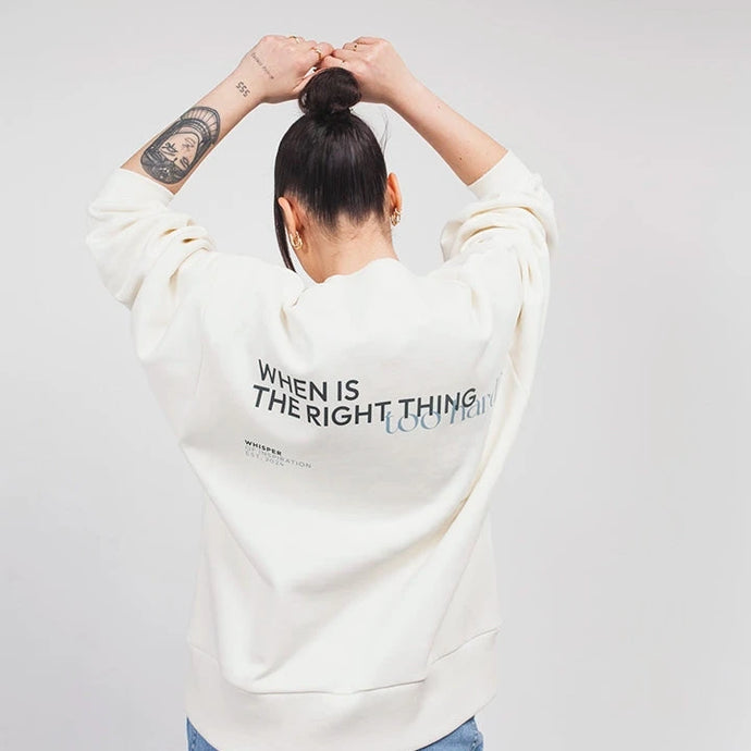 Model in Rückenansicht trägt den cremefarbenen Whisper of Inspiration Sweater mit Backprint und erhobenen Armen vor hellem Studiohintergrund.