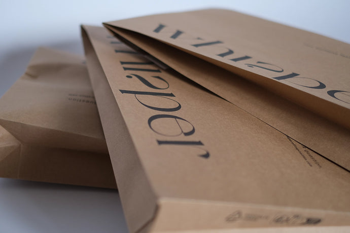 Gestapelte braune Verpackungen von Whisper of Inspiration mit schwarzem Logodruck in einer Nahaufnahme.